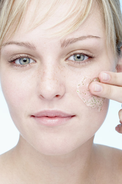 Young woman applying exfoliating gel to face, portrait, close-up